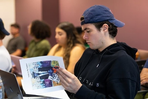 A student holding and reading a course packet that features art including Glenn LigonUntitled (I Am a Man)